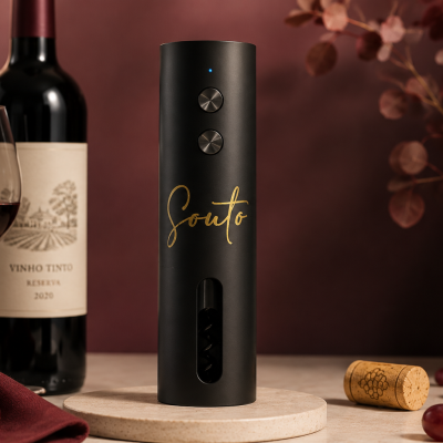 Abridor de garrafas preto com escrita dourada Souto, garrafa de vinho tinto reserva 2020, copo de vinho, uvas, e vaso com folhas secas.