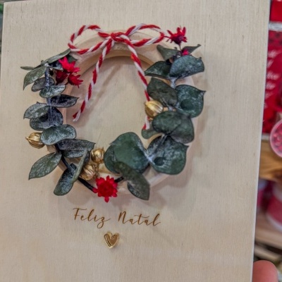 Quadro decorativo natalício com coroa de folhas e flores e texto Feliz Natal