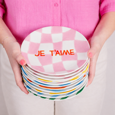 Pratos cerâmicos coloridos com texto JE TAIME segurados por mãos