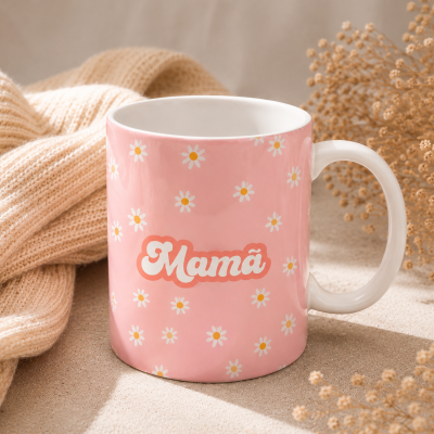 Caneca rosa com flores margaridas e a palavra Mamã com tecido de malha bege ao lado e flores secas ao fundo
