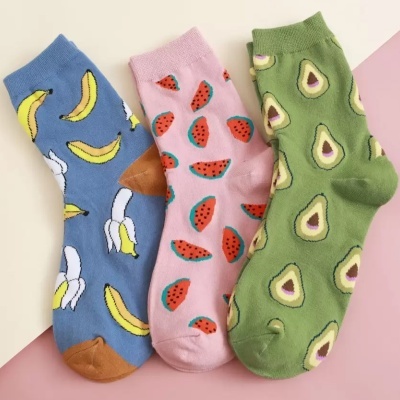 Três pares de meias coloridas com padrões de frutas sobre superfície clara e rosa.