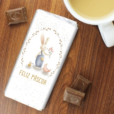 Embalagem de chocolate branca com coelho e texto FELIZ PÁSCOA sobre madeira com chocolate e chá