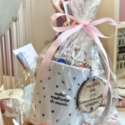 Caneca branca com corações e texto, embrulhada em celofane com fita rosa e pendente de madeira
