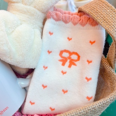 Meia branca com corações cor de laranja, fita e bordas rosa numa cesta de juta