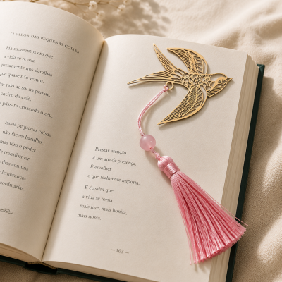 Marcador de páginas dourado em forma de pássaro com tassel rosa num livro aberto