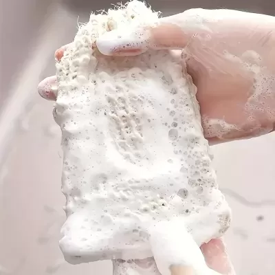 Mão segurando esponja porosa bege com espuma branca
