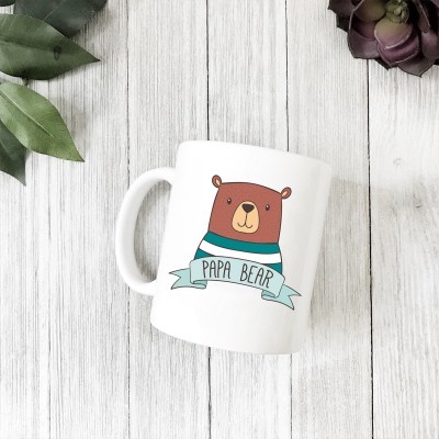 Caneca branca com desenho de urso e texto 'PAPA BEAR' sobre mesa de madeira clara