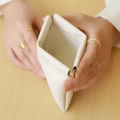 Carteira branca pequena com fecho dourado segurada por mãos com anéis finos