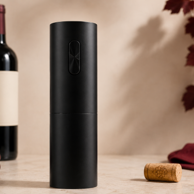 Abridor de vinho elétrico preto cilíndrico com garrafa de vinho, taça, uvas, rolha e pano ao fundo