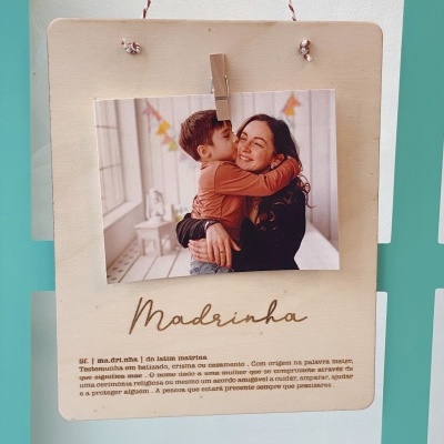 Placa de madeira clara com foto de mulher e criança e texto 'Madrinha' pendurada por cordão vermelho e branco