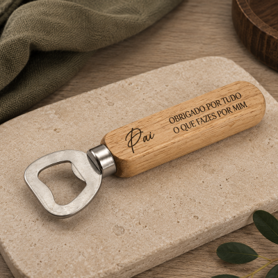Abridor de garrafas com pega de madeira clara gravado com texto para pai, sobre base de pedra e superfície de madeira.