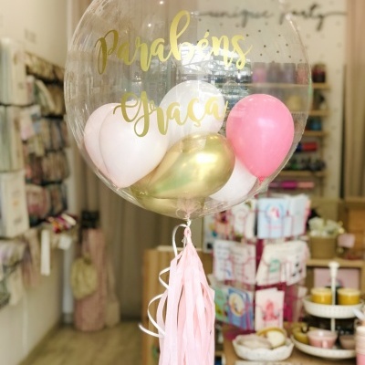 Balão transparente grande com texto dourado e balões coloridos dentro, pendurado em loja