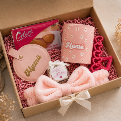 Caixa de presente com artigos cor de rosa para mãe, incluindo caneca, porta-moedas e máscara de colagénio para olhos.