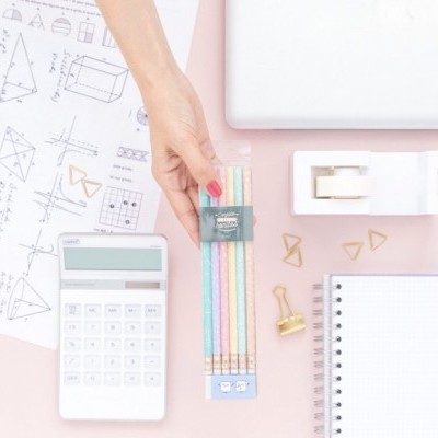 Material escolar e escritório organizado sobre superfície rosa com calculadora, lápis coloridos, bloco de notas e acessórios.