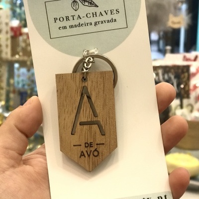 Porta-chaves em madeira gravada com texto 'A DE AVÔ' e cartão com inscrição promocional.