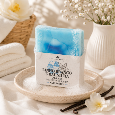 Sabonete azul em embalagem branca com texto sobre prato bege com espuma, flores e toalhas ao fundo
