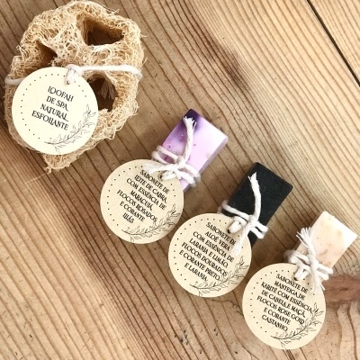 Esponja natural e quatro sabonetes artesanais com etiquetas, sobre madeira clara