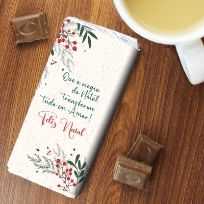 Barra de chocolate com embalagem natalícia decorada e texto em português ao lado de pedaços de chocolate e chávena