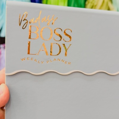 Planner semanal cinzento com texto dourado e faixa ondulada branca