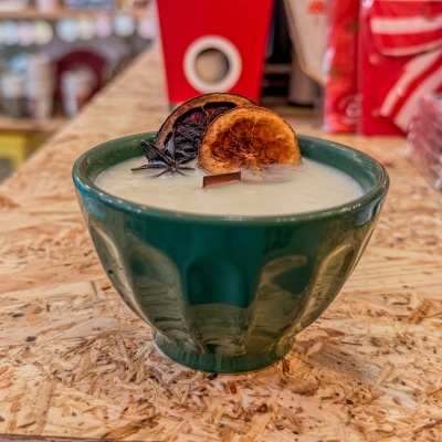 Vela branca numa tigela verde com decoração de anis e frutas desidratadas sobre mesa de madeira