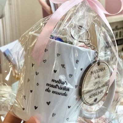 Caneca branca com corações pretos e texto para madrinha, embalada com fita rosa e porta-chaves redondo em madeira