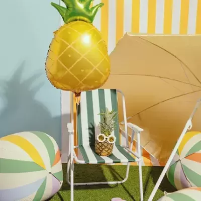 Cadeira com tecido verde e branco e abacaxi com óculos, balão de abacaxi, guarda-sol e bolas de praia coloridas