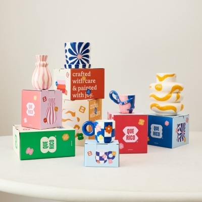 Cerâmicas coloridas sobre caixas com texto QUE RICO e crafted with care & painted with joy.