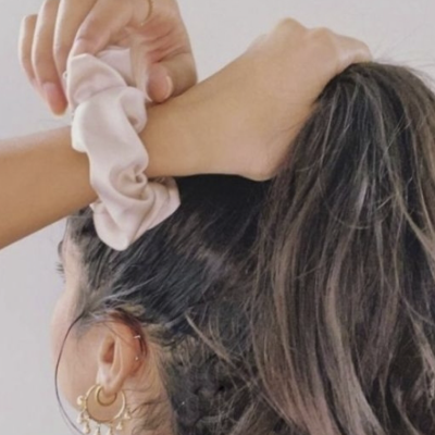 Scrunchie rosa claro acetinado em cabelo castanho escuro com brincos dourados