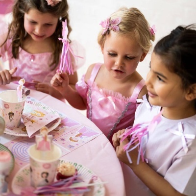 Três meninas numa festa infantil com decoração rosa e guardanapos e copos com bailarinas.