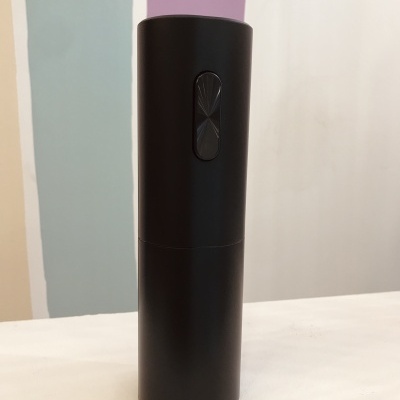 Dispositivo preto cilíndrico com botão, sobre superfície branca e fundo colorido