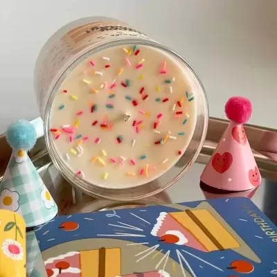 Vela branca com confetes coloridos numa bandeja com chapéus de festa e cartão colorido