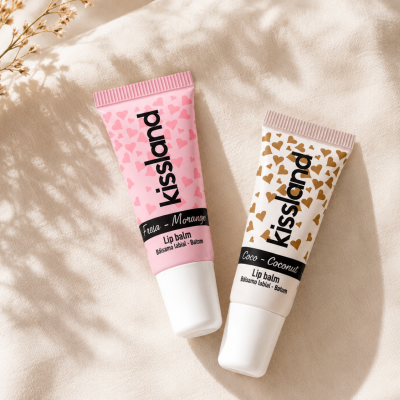 Dois tubos de bálsamo labial Kissland rosa e branco com corações sobre tecido bege claro.