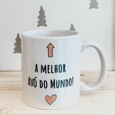 Caneca branca com texto A MELHOR AVÓ DO MUNDO e símbolos de seta e coração, sobre mesa de madeira clara
