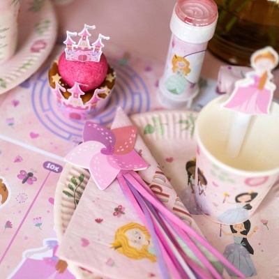 Artigos de festa infantil com tema de princesas, incluindo cupcake, tubo, copo e guardanapos cor-de-rosa e lilás.