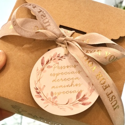 Caixa de presente castanha com fita bege e etiqueta floral com texto dourado