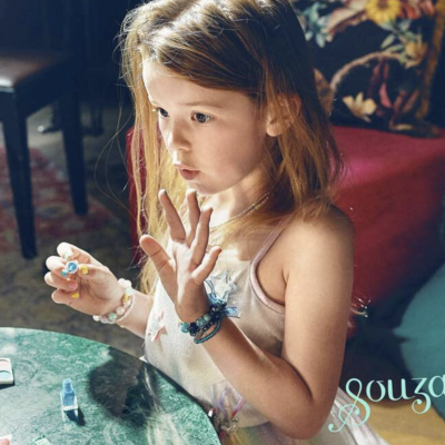 Menina sentada com vestido branco brincando numa mesa verde com materiais de pintura