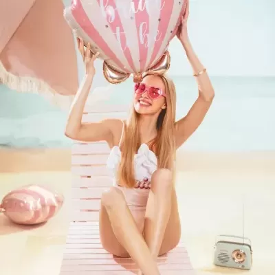 Mulher na praia com fato de banho e balão rosa e branco com texto bride to be