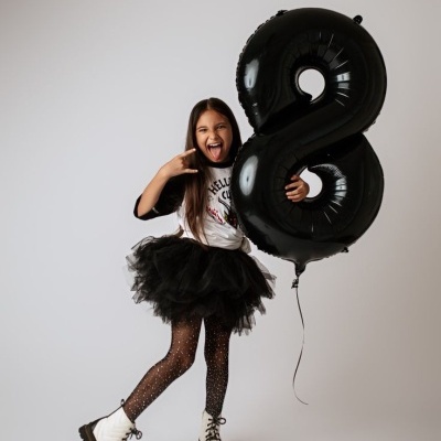 Criança com roupa preta e branca segurando balão número 8 preto