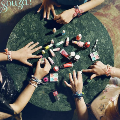 Mesa redonda com vernizes e sombras de olhos e mãos de crianças com pulseiras coloridas