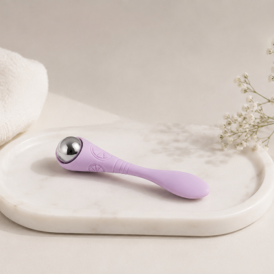 Aparelho de massagem roxo com esfera metálica numa bandeja de mármore