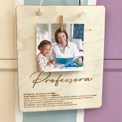 Placa decorativa de madeira com foto e texto 'Professora', pendurada numa parede colorida.