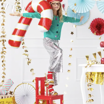 Criança com roupa colorida e balão de Natal insuflável em ambiente festivo decorado