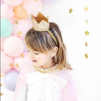 Menina com capa rosa e coroa dourada com balões coloridos ao fundo