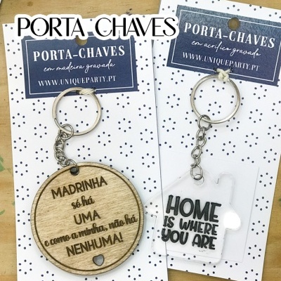 Dois porta-chaves, um em madeira redondo gravado e outro acrílico transparente em forma de casa com texto preto.