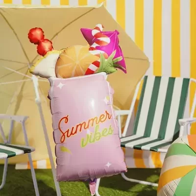 Balão cor-de-rosa em forma de copo com texto Summer Vibes decorado com frutos e guarda-chuva num ambiente de verão.