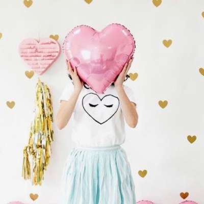 Pessoa com almofada coração cor de rosa, t-shirt branca com coração preto e saia azul clara