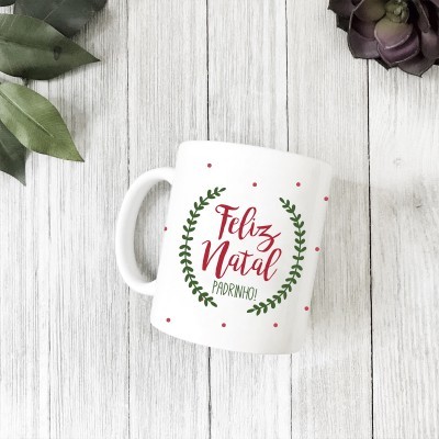 Caneca branca com mensagem de Natal em verde e vermelho sobre madeira clara