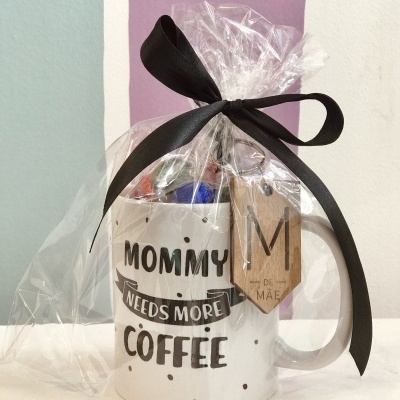 Caneca branca com texto preto e bolinhas, embrulhada em celofane com fita preta