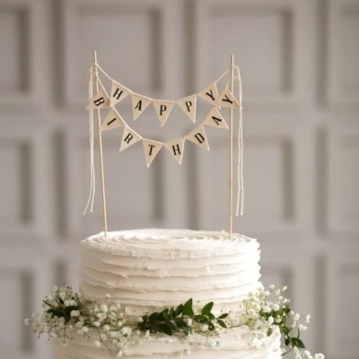 Bolo branco decorado com bandeirolas HAPPY BIRTHDAY no topo e flores ao redor.