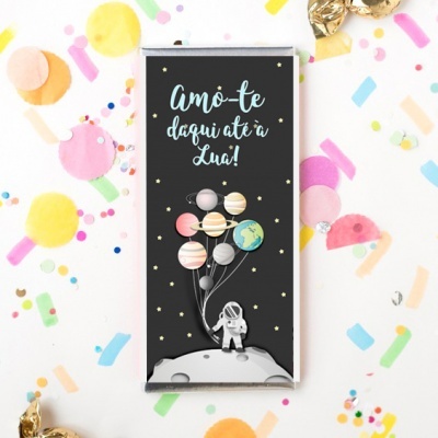 Embalagem de chocolate com astronauta e balões planetas, texto 'Amo-te daqui até à Lua!' em fundo preto.